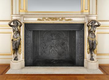 Chimneypiece with two bronze female figures on either side and gilt firedogs in the middle. A c…